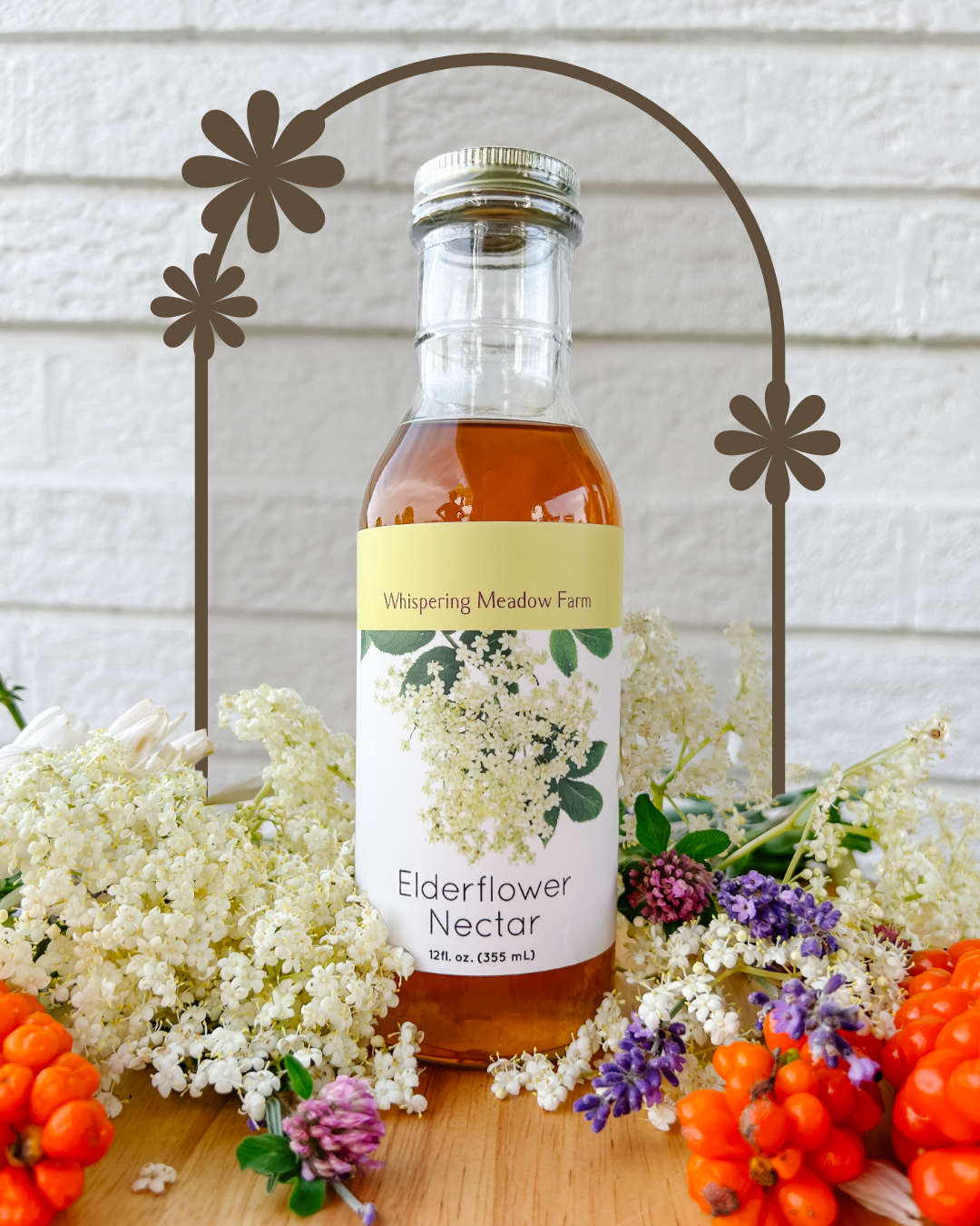 Bright Orange Elderflower Nectar Bottle placed among light purple flowers, white elderflowers, and bright red berries.